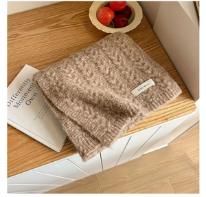 Close-up of brown cable-knit wool scarf with branded label on a wooden desk