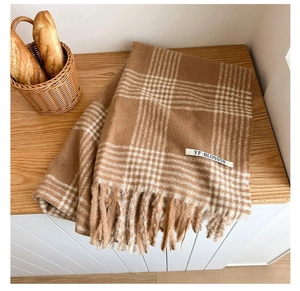 Detailed texture of caramel houndstooth scarf with tassels and brand tag on wood table