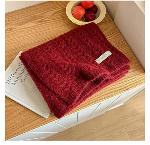 Macro view of burgundy knitted scarf with thick cable pattern on a wooden desk
