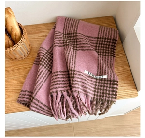 Close-up of soft houndstooth cashmere scarf with fringe and brand label on a wood table