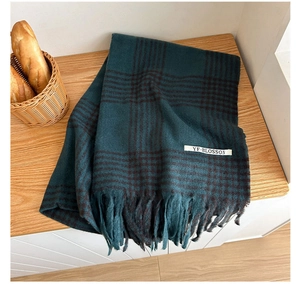 Detail of dark green houndstooth scarf featuring tassel edges and a sewn-on brand label