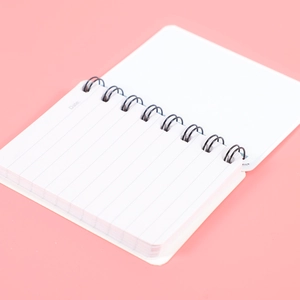 Portable A7 coil notebook with lined paper and date header on a soft pink background