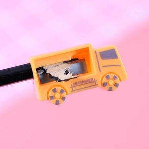Yellow school bus pencil sharpener with manual blade and pencil shavings on pink background