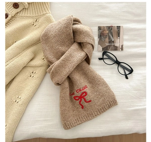 Detail van beige gebreide sjaal met rode Cool Chill tekst en geborduurde strik
