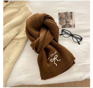 Detail van gebreide sjaal met La Challe borduursel en witte strik op bruine wol