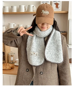 Détail d'une écharpe gris clair avec bordure foncée et casquette marron brodée