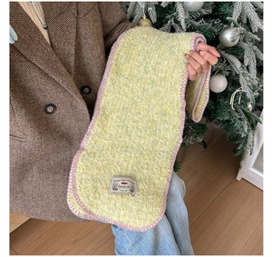 Détail d'une écharpe en maille jaune avec bordure violette et étiquette décorative