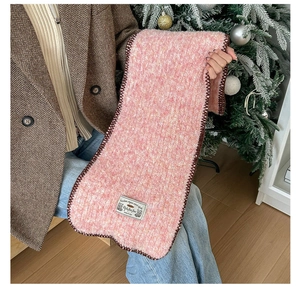 Gros plan sur l'écharpe en tricot rose avec bords festonnés marron et étiquette décorative