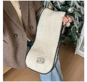 Détail d'une écharpe en peluche crème avec coutures noires contrastées et écusson tigre