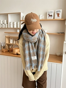 Detail of blue and brown plaid scarf with fringe and a Malibu embroidered baseball cap