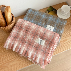 Close-up of thick plaid scarves with tassels and brand label on a wooden surface