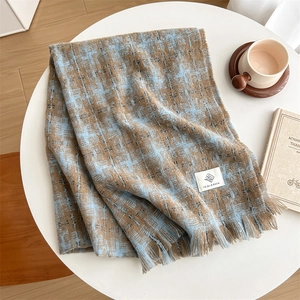 Blue and brown plaid cashmere scarf with fringes and logo on a cozy table setting