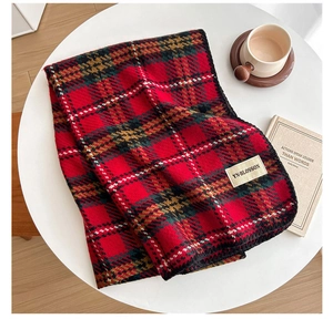 Detail of red and green plaid scarf texture with woven label on a white surface