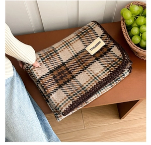 Detail of plaid scarf featuring brown crochet edges and a minimalist brand label