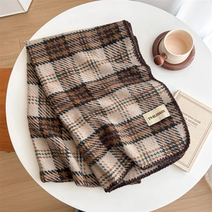 Retro plaid knit scarf in brown and beige tones with stitched brand label on white table