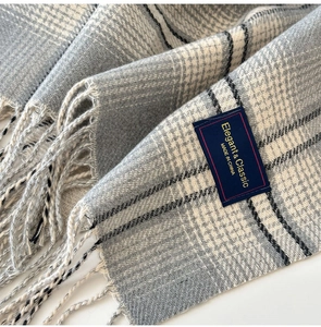 Detail of grey plaid scarf showing soft texture, long tassels and woven label