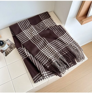Détail d'une écharpe à carreaux marron café avec de longues franges sur fond neutre