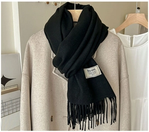 Gros plan d'une écharpe noire aspect cachemire avec franges et étiquette tissée sur manteau