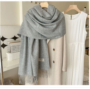 Détail d'une écharpe en maille gris clair avec de longues franges sur un cintre