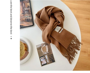 Detail of 100% pure wool caramel scarf featuring soft fringes and a white woven label