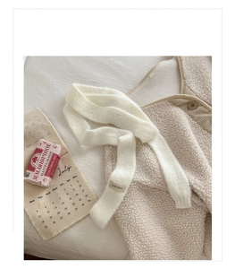 Dettaglio di una sciarpa in maglia bianca con etichetta Vegetable su un gilet in pile