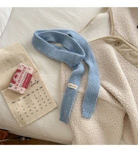 Dettaglio sciarpa in maglia azzurra con etichetta tessuta VEGETABLE su tessuto bianco