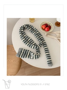 Detail of grey and white striped knit scarf with decorative label on a white table