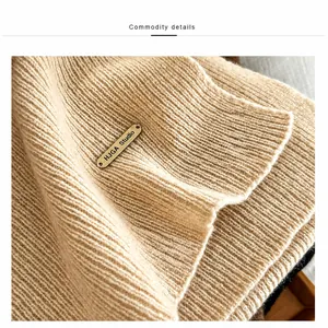 Close-up of ribbed 100% wool knit scarf in light camel with a gold metal logo plate