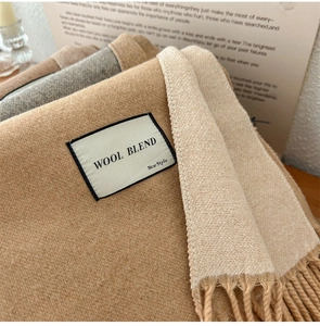 Detailed close-up of wool blend fabric texture and sewn label on camel fringe scarf