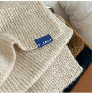 Dettaglio di sciarpe in maglia spessa beige, marrone e nero con etichetta in tessuto