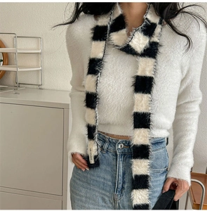 Détail d'une écharpe étroite en peluche à damier portée sur un pull blanc avec élégance