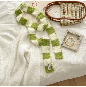 Détail de l'écharpe en tricot pelucheux vert et blanc montrant la texture et l'étiquette