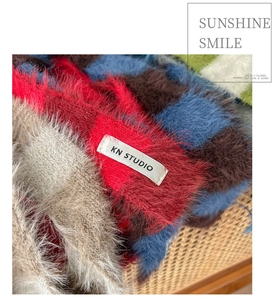 Détail macro de l'écharpe en peluche à carreaux avec étiquette KN STUDIO et maille douce