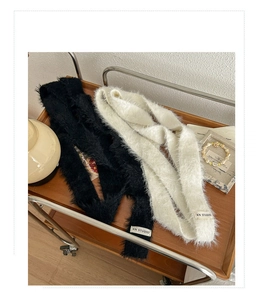 Detailed view of fluffy black and cream knit scarves with brand labels on wooden tray