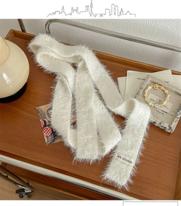 Detail of soft white plush scarf with KN STUDIO woven label on a rustic wooden tray