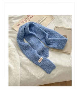 Dettaglio della sciarpa in peluche blu con etichetta del marchio su sfondo morbido