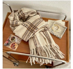 Detail van beige en bruine geruite sjaal met dikke franjes op een houten dienblad