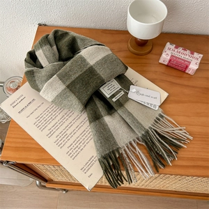 Detail of 100% pure wool scarf with green plaid pattern and tassel trim on wood surface