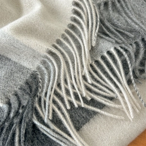 Macro detail of high-quality wool blend scarf featuring soft tassels and grey plaid texture