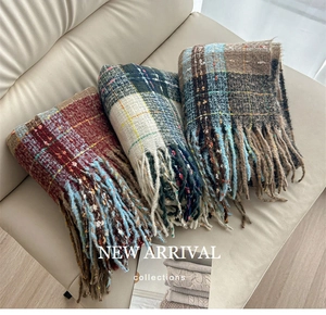 Detailed view of three warm plaid scarves with tassels on a soft leather sofa
