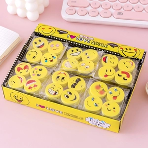 Macro shot of circular smiley emoji erasers set in a yellow box on a pink desk