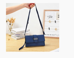Petit sac enveloppe bleu marine en similicuir avec détails métalliques tenu à la main
