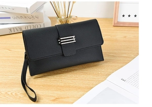 Gros plan de la pochette enveloppe noire en cuir grainé avec détails argentés sur bois