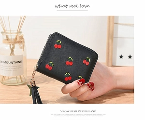 Detailed close-up of a black leather wallet with cherry embroidery and tassel star charm