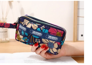 Détail d'une pochette en nylon fleurie avec trois compartiments zippés et dragonne assortie