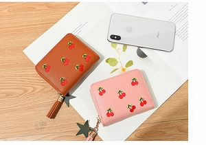 Detail of zip-around wallets with cherry embroidery and star tassel on a wooden desk