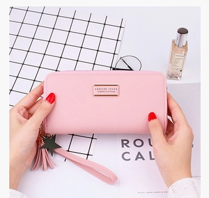 Pink long wallet with tassel and wristlet held by hands in a stylish setting