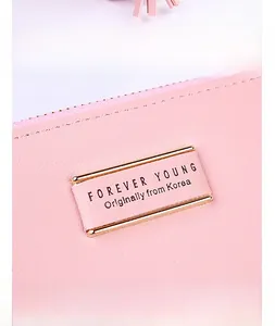 Detailed close-up of pink pebbled leather wallet with a gold Forever Young metal plate