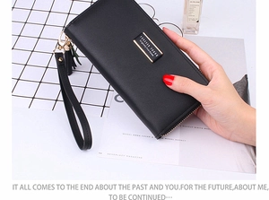 Detailed view of a long black zip-around wallet with wristlet strap and decorative tassel