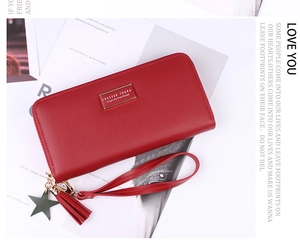 Detail of red faux leather long wallet with zipper, tassel charm and metal logo plate